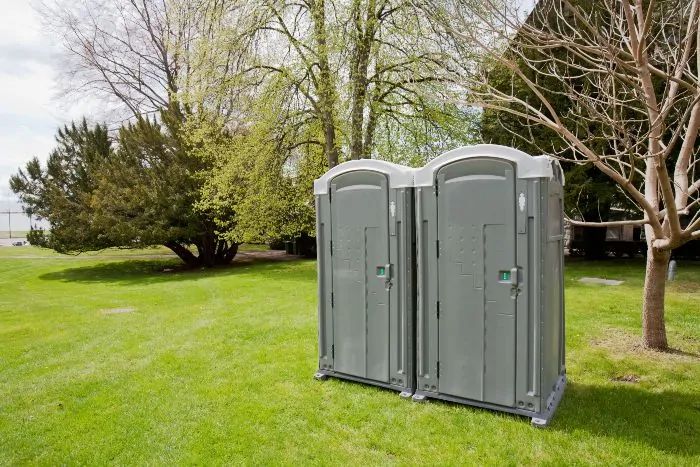 Two gray portable restrooms were placed on a green lawn for event needs in Rancho Cordova, CA.